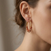 A close-up of a woman's ear wearing a gold hoop earring adorned with small red beads along the lower curve, against a soft neutral background.