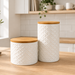 Two white textured ceramic canisters with light wood lids, displayed on a wooden kitchen countertop.