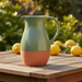 Green and terracotta ceramic pitcher on a wooden table with lemons