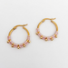 A pair of gold hoop earrings with a light Lilac braided cord detail and small gold beads along the bottom, displayed on a neutral light gray background.