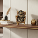 Decorative monkey figurine with sunglasses and a drink on a chair, placed on a wooden shelf.